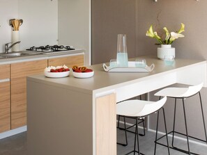 A modern kitchen with a central island, white bar stools, and a vase with flowers. - Comfortable mobile home with terrace in Saint-Jean-de-Monts (Saint-Jean-de-Monts)