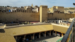A view of a courtyard with traditional tiled roofs and a large wall with a tower. - RIAD RAHBA FEZ (Fes)
