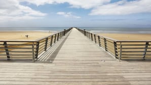 Een houten vlonder die naar een strand loopt, met een heldere lucht.