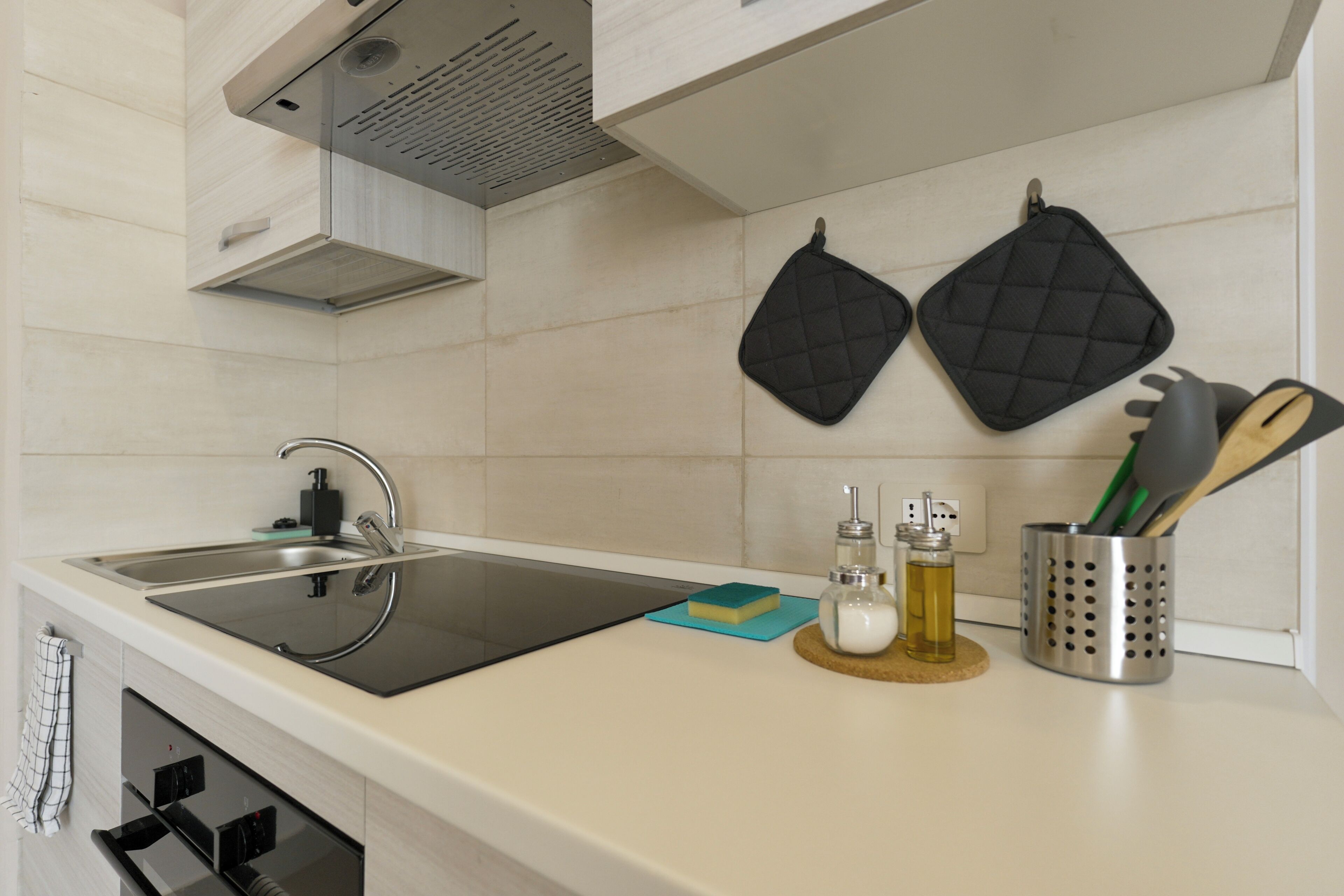 A kitchen with a stainless steel sink, black cutting board, and a utensil holder.