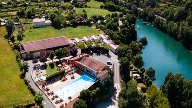 En vy från ovan av ett hotell med en swimmingpool, omgivet av grönska och en flod.