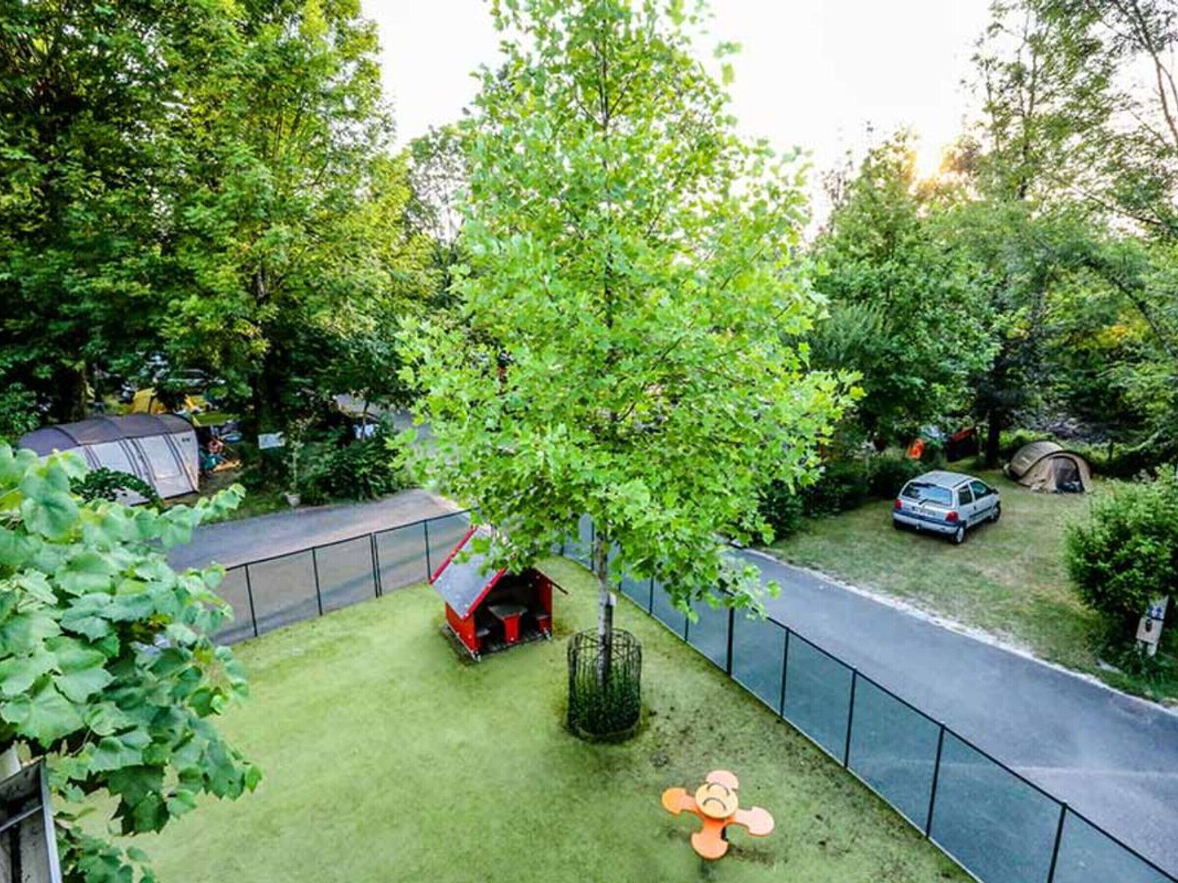 A fenced outdoor area with a tree, a tent, and a car.