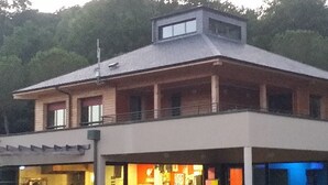Un edificio con tetto piatto e un balcone. Ci sono persone sedute all'esterno.