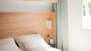 Una cama bien hecha con cabecera de madera, una mesita de noche con lámpara y una ventana con cortinas.