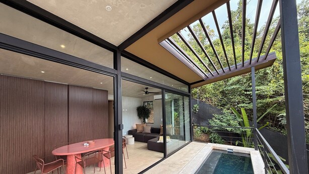 A modern interior with a glass-enclosed dining area, a pool, and a view of lush greenery.