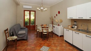 Una cucina compatta con zona pranzo, mobili bianchi, pavimento piastrellato e ventilatore a soffitto.