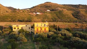 Un edificio giallo con un balcone, immerso nel verde e con colline sullo sfondo.