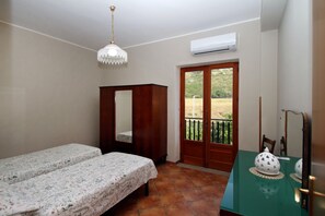 A room with two beds, a wooden wardrobe, a table with a decorative bowl, a hanging light fixture, and a sliding glass door leading to an outdoor area. - Il Giardino al Mare di Anna is an apartment located on the third and top floor of an old manor house, surrounded by the countryside of the Piana di Caronia and just a few steps from the sea.The apartment features a spacious kitchen-living area with a sof (Marina di Caronia)
