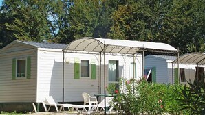 En række huse med mobilt hjem, grønne skodder, en overdækket terrasse og grusbelagt jord.