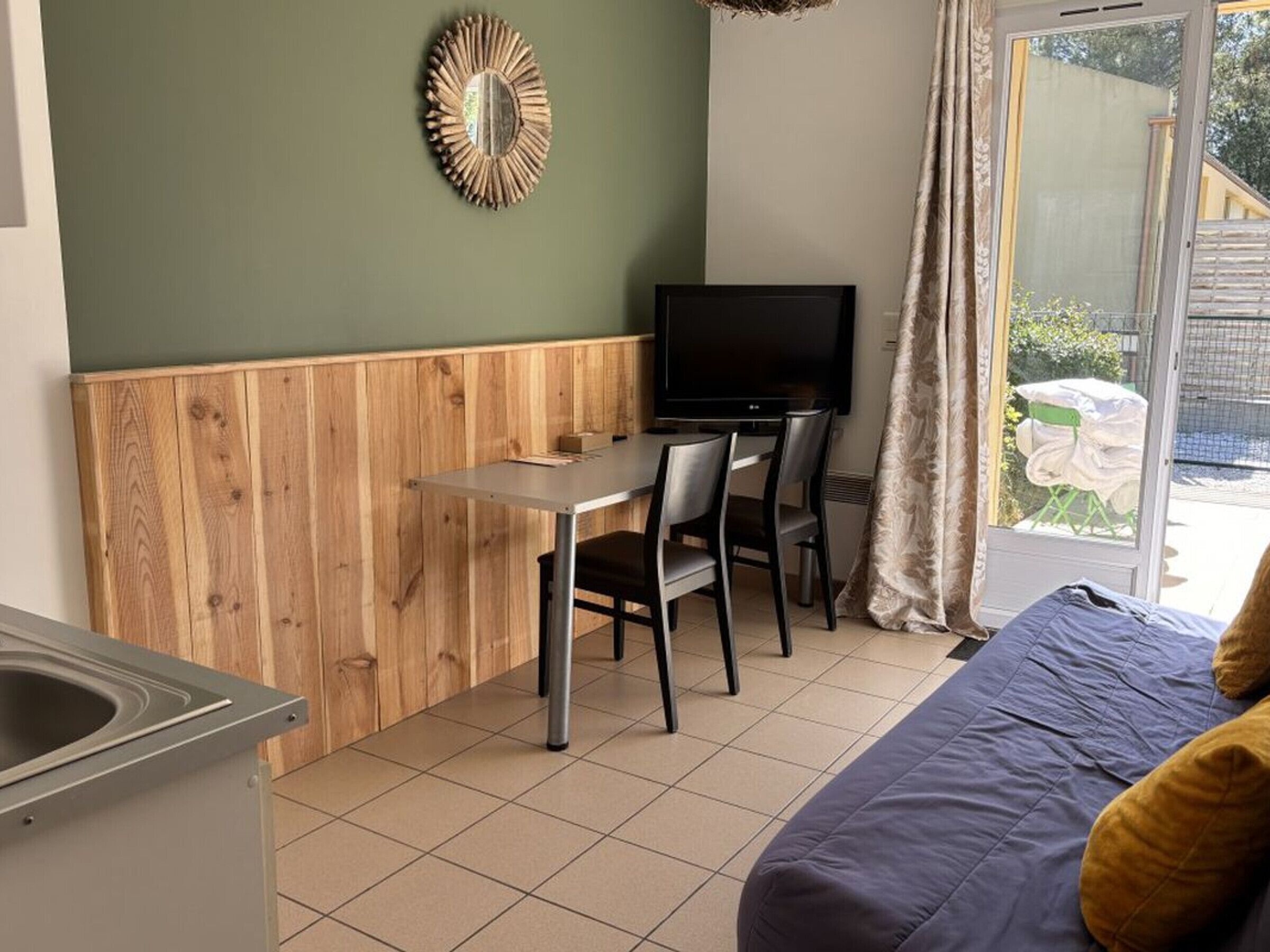 Una habitación con una cama, televisión, mesa y sillas, y ventana con cortinas.