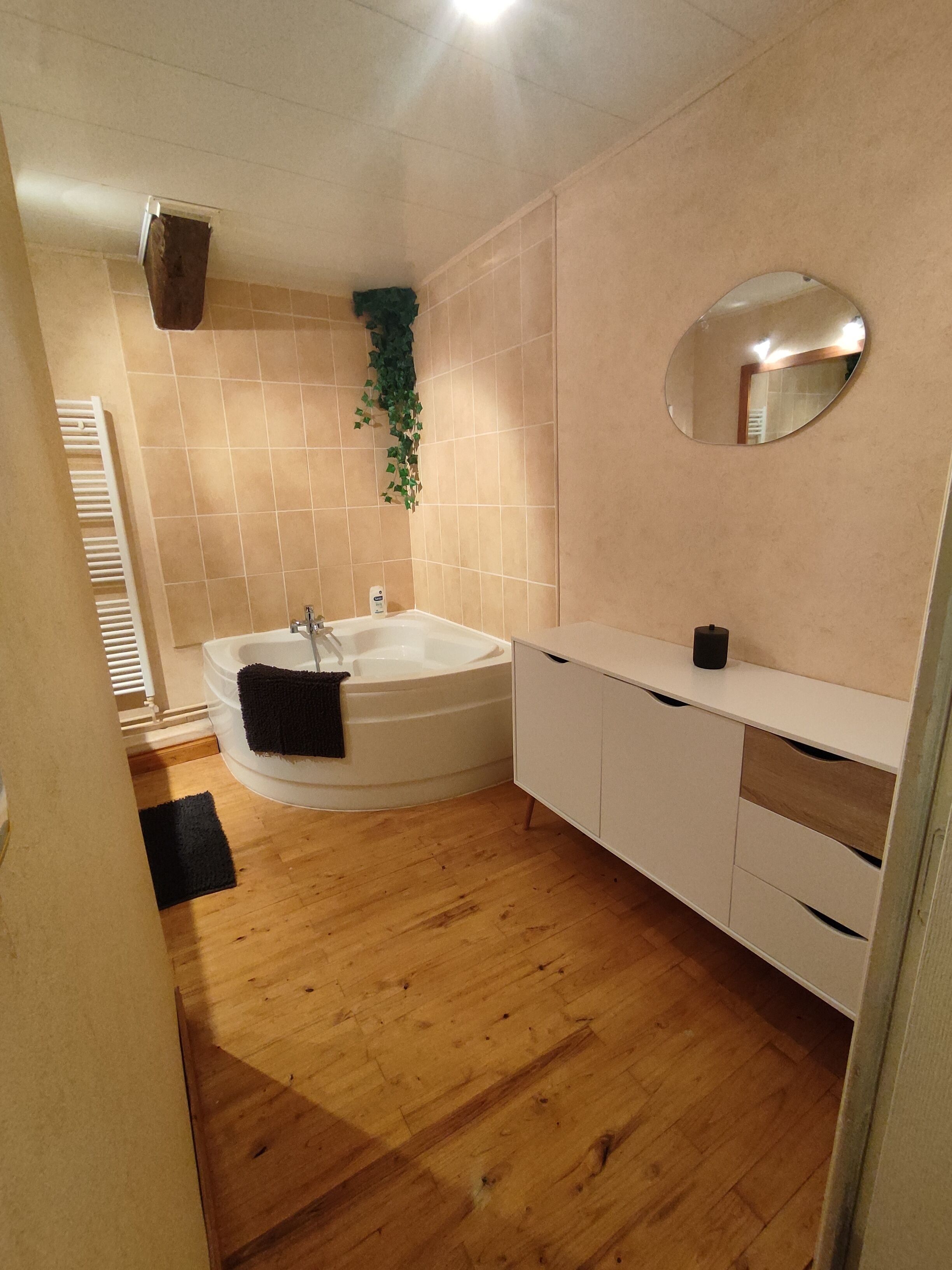 Un baño con bañera, tocador blanco, espejo y suelo de madera.