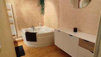 Un baño con bañera, tocador blanco, espejo y suelo de madera.