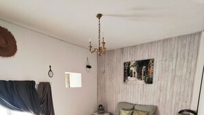 Ein Schlafzimmer mit einem großen Bett, Holzboden, einem gemusterten Teppich, einem Nachttisch, einem Sessel, einem Deckenventilator und einem Fenster mit Vorhängen.