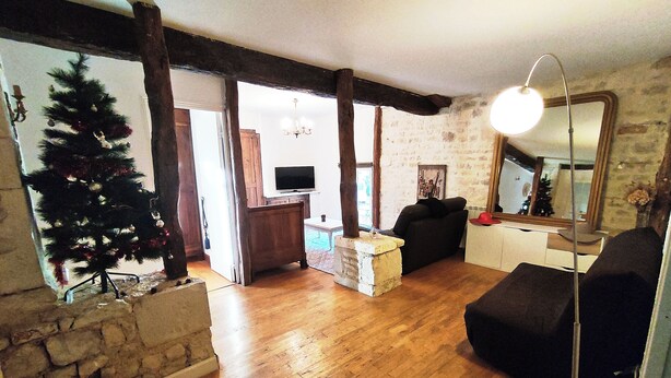 Ein gemütliches Wohnzimmer mit Holzboden, Steinwand, Weihnachtsbaum, schwarzem Sofa, Fernseher und Spiegel.