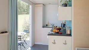 A compact kitchen with a built-in stove, a small sink, and a countertop with various items. There is a dining area with a table and chairs visible through an open door. - Cozy Mobile Home with Terrace in Roquebrune-sur-Argens (Roquebrune-sur-Argens)