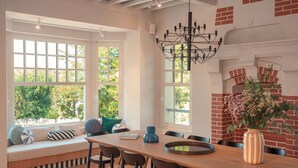 A dining area with a wooden table, chairs, and a bench with cushions. There are large windows with a view of greenery outside. - Villa des Reves Luxury in Villers Pool Jacuzzi Padel Court Close to Deauville (Villers-sur-Mer)