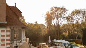 A building with a stone facade and a sloped roof, a swimming pool, outdoor seating, and a well-maintained garden. - Villa des Reves Luxury in Villers Pool Jacuzzi Padel Court Close to Deauville (Villers-sur-Mer)