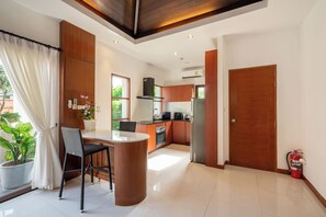 Una cocina moderna con armarios de madera, una isla central y una zona de comedor con una silla y una mesa.