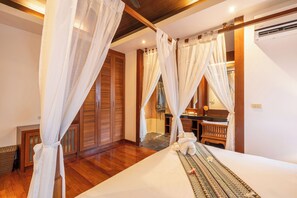 A hotel room with a bed, wooden floor, white curtains, a bathroom with a shower, and a vanity. - Villa Amida • Balinese Pool Villa • Big Sala & Terrace • Nai Harn & Rawai Beach (Tambon Rawai)