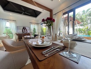 A dining area with a table set for two, a television, and a view of the outdoors. - Villa Amida • Balinese Pool Villa • Big Sala & Terrace • Nai Harn & Rawai Beach (Tambon Rawai)