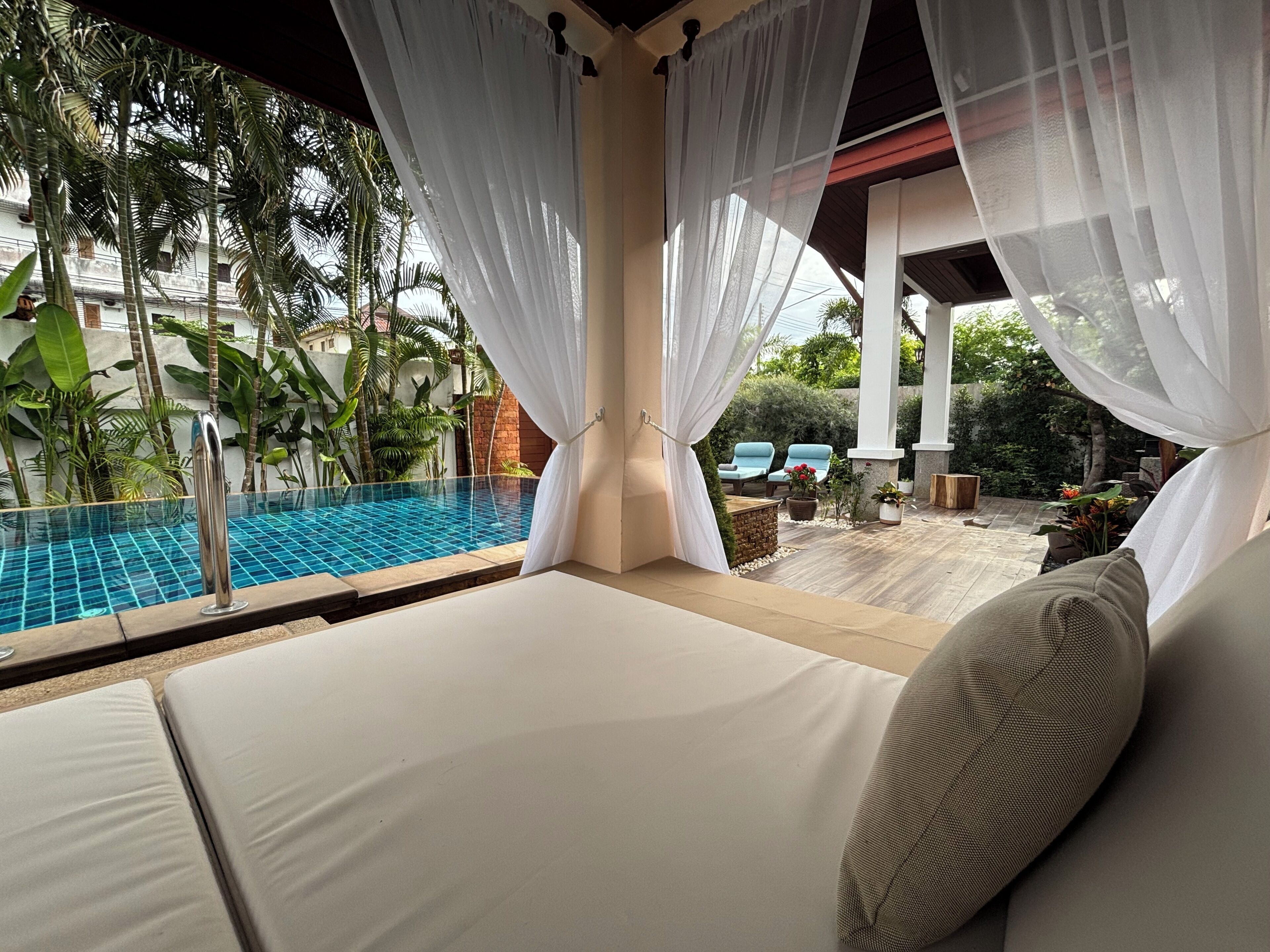 A poolside area with a glass-tiled pool, white curtains, and lounge chairs.