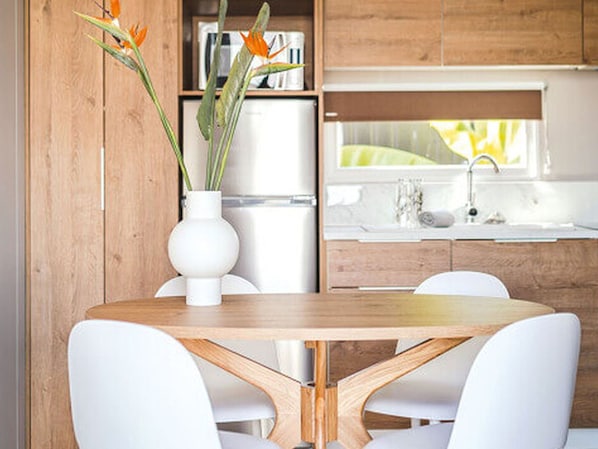Une cuisine moderne avec des meubles en bois, un réfrigérateur blanc, un évier blanc et une table à manger avec des chaises blanches.