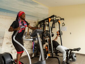 Une salle de sport équipée d’un tapis de course, de matériel de musculation, et où une personne s’entraîne sur le tapis de course.