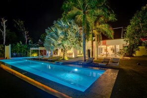 Una piscina con sillas de descanso, palmeras y un edificio moderno al fondo.