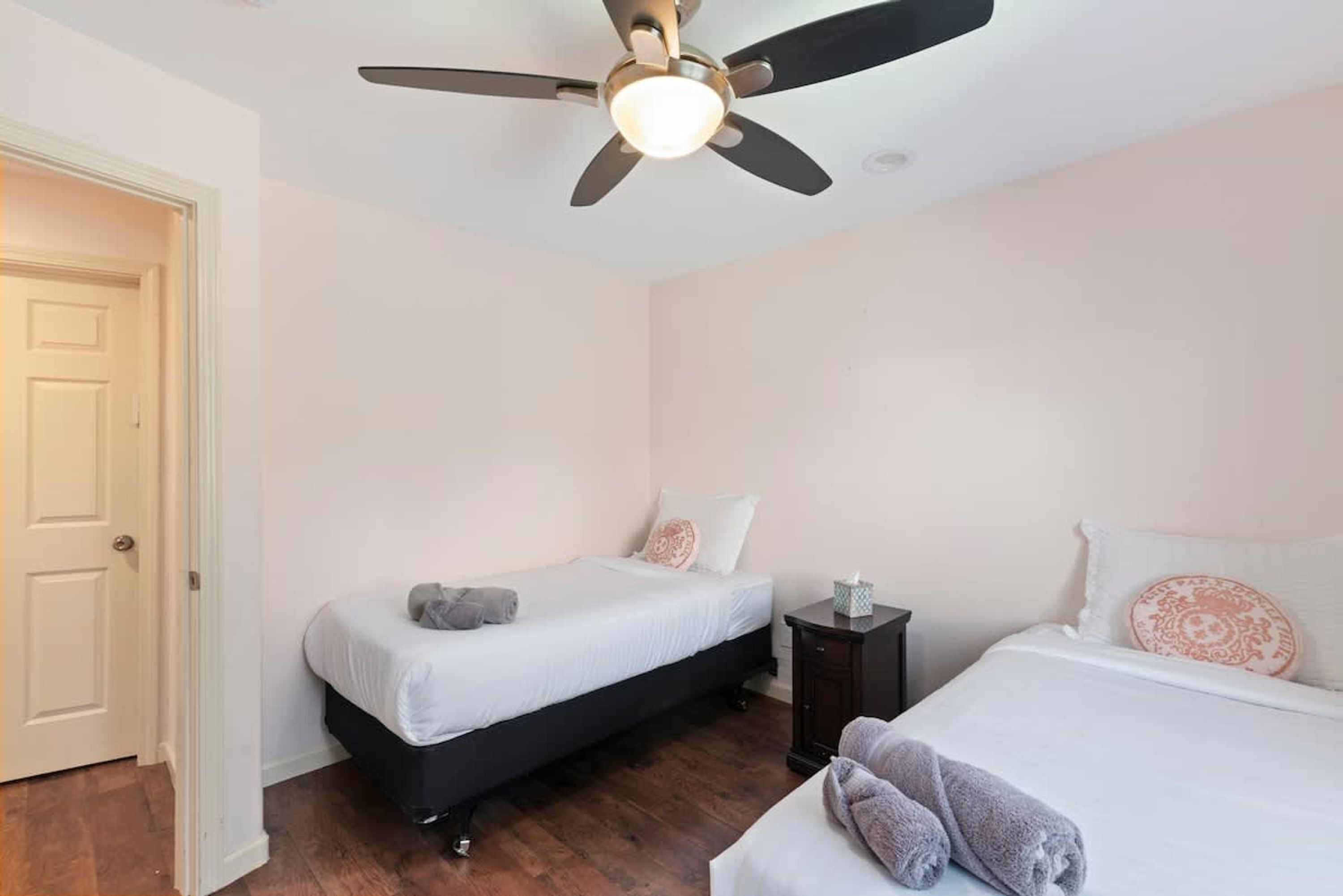 Une chambre avec deux lits, un ventilateur de plafond et une table de chevet.