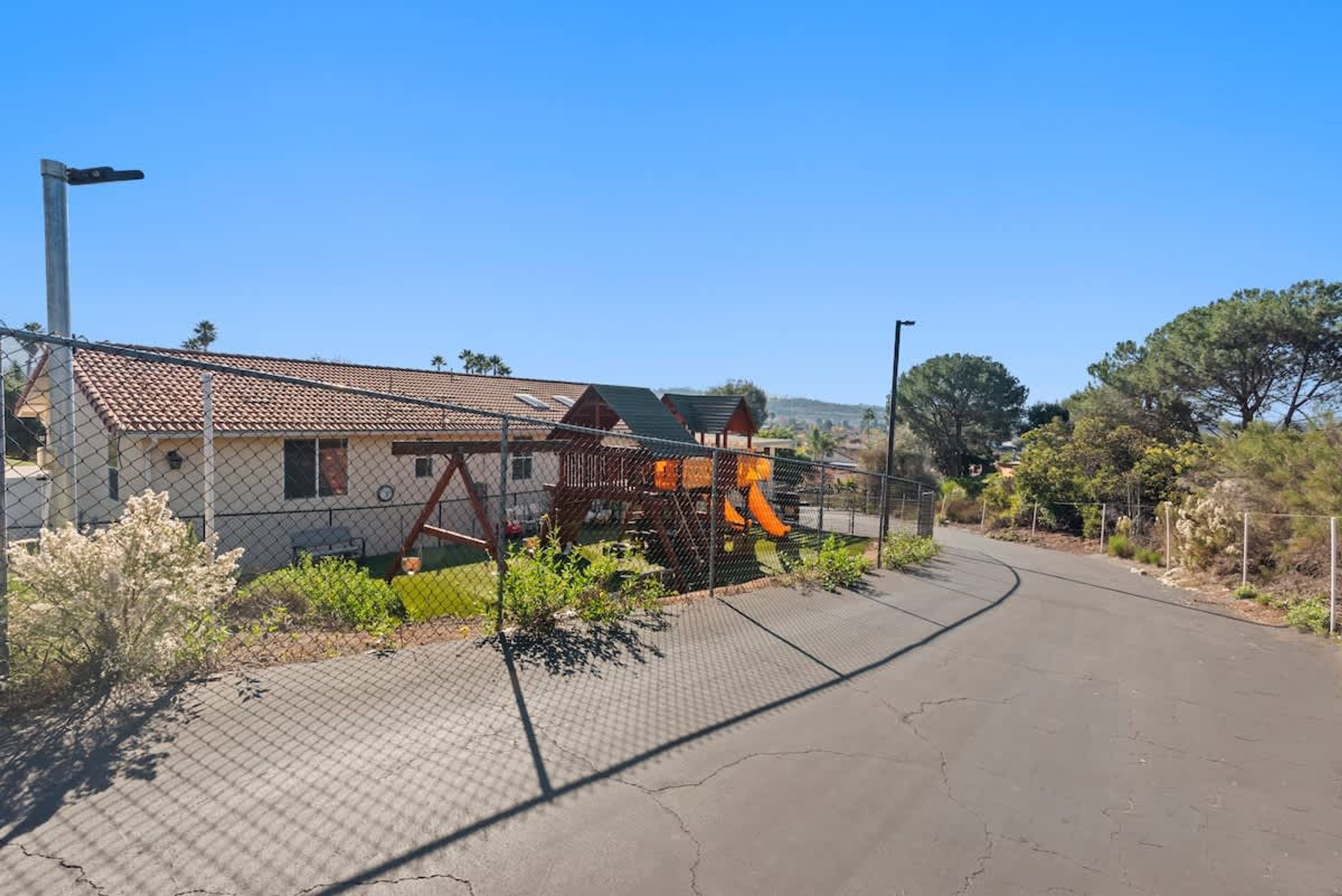 A fenced property with a playground, a house with a tiled roof, and a clear sky.