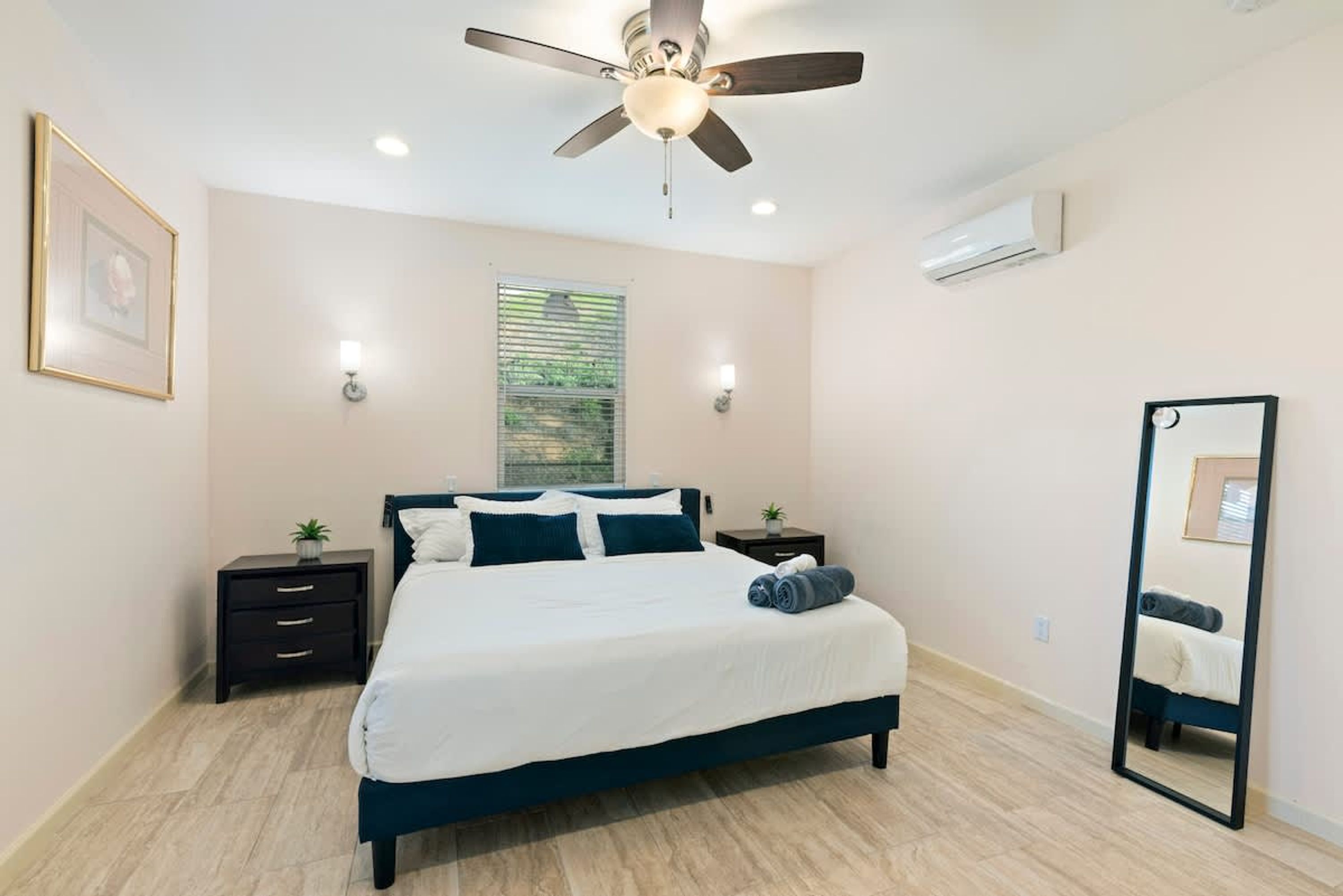 A bedroom with a bed, a ceiling fan, a window, a nightstand, and a mirror.