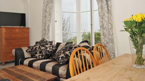 A living room with a sofa, wooden table, and a television on a dresser. - Violet's Rest (Exeter)
