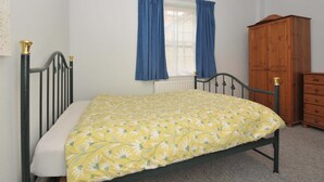 A bedroom with a bed, a window with curtains, a wooden wardrobe, and a radiator. - Violet's Rest (Exeter)