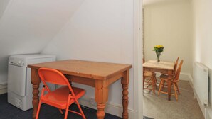 A room with a wooden table and orange chair, a radiator, and a washing machine. - Violet's Rest (Exeter)