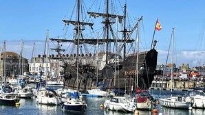 A marina with multiple boats docked, including a large ship with masts and flags.
