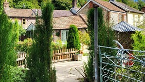 A traditional stone house with a tiled roof, surrounded by lush greenery and a wooden fence.