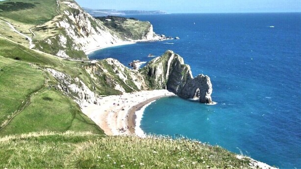 A coastal landscape with a beach, cliffs, and a clear blue sea.