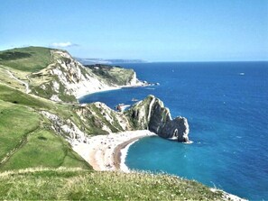 A coastal landscape with a beach, cliffs, and a clear blue sea.