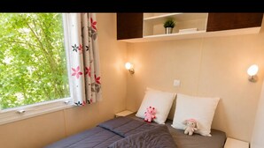 Une chambre à coucher avec un lit, deux tables de chevet, une fenêtre avec des rideaux et une étagère sur laquelle est posée une plante.
