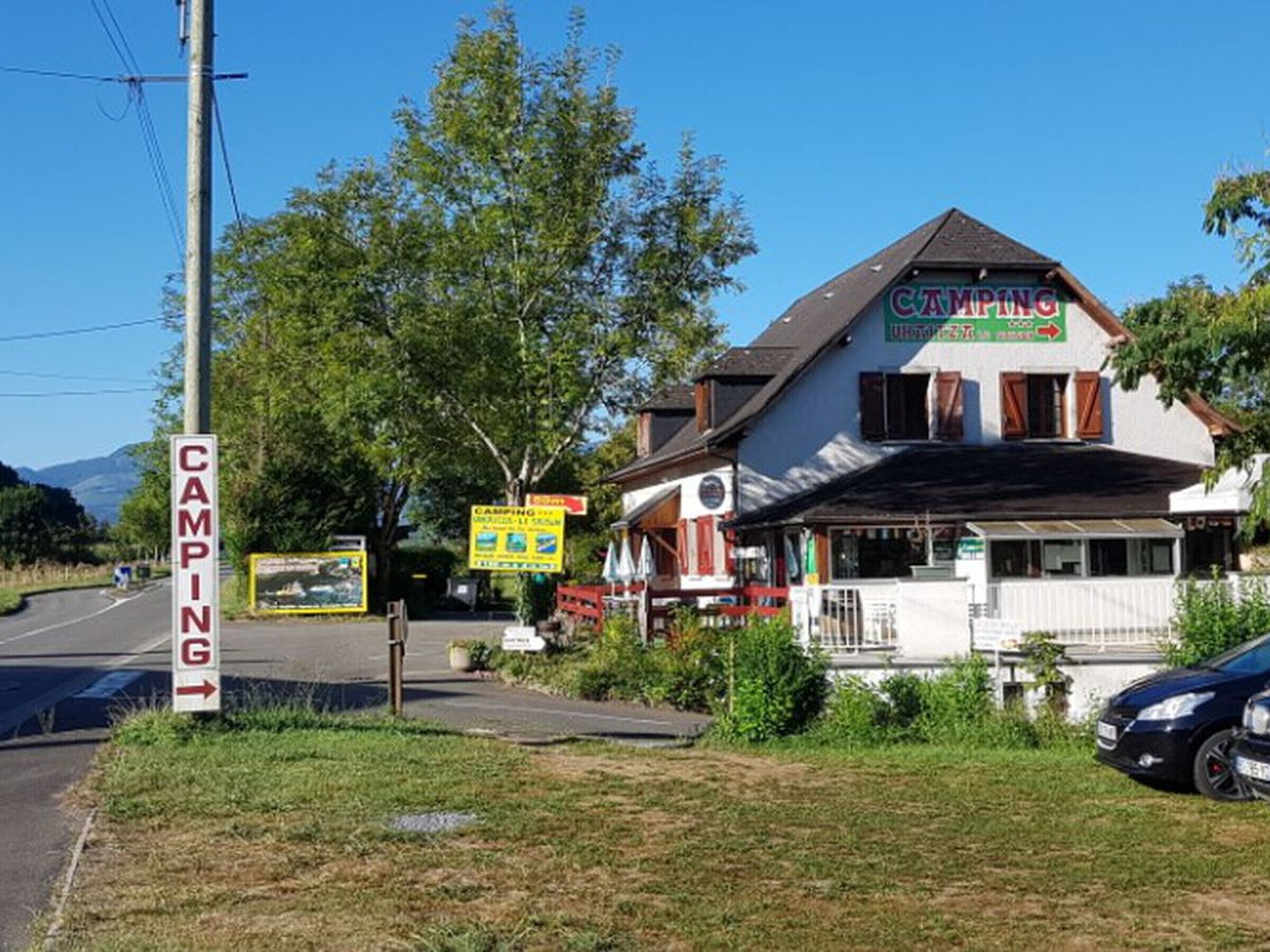 A building with a 'CAMPING' sign, a road sign indicating a camping area, and a car parked in front.