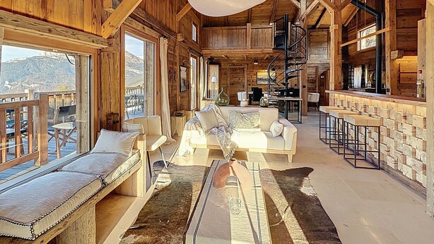 Un interior espacioso de madera con zona de comedor, un conjunto de sofás y una escalera que lleva a un nivel superior.