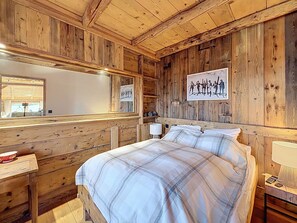 A wooden cabin room with a bed, a nightstand, a mirror, and a wall-mounted picture. - Chalet with 5 bedrooms + dormitory near Combloux slopes (Combloux)