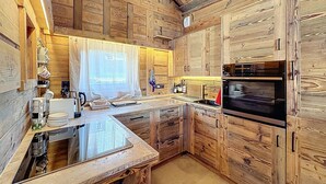 Una cocina rústica con armarios de madera, horno empotrado y un amplio ventanal con cortina translúcida.