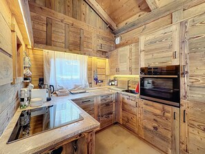 A rustic kitchen with wooden cabinetry, a built-in oven, and a large window with a sheer curtain. - Chalet with 5 bedrooms + dormitory near Combloux slopes (Combloux)