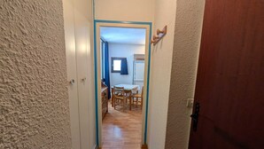 Kapea käytävä, jossa on puulattia, johtaa ruokailutilaan, jossa on pöytä ja tuoleja.