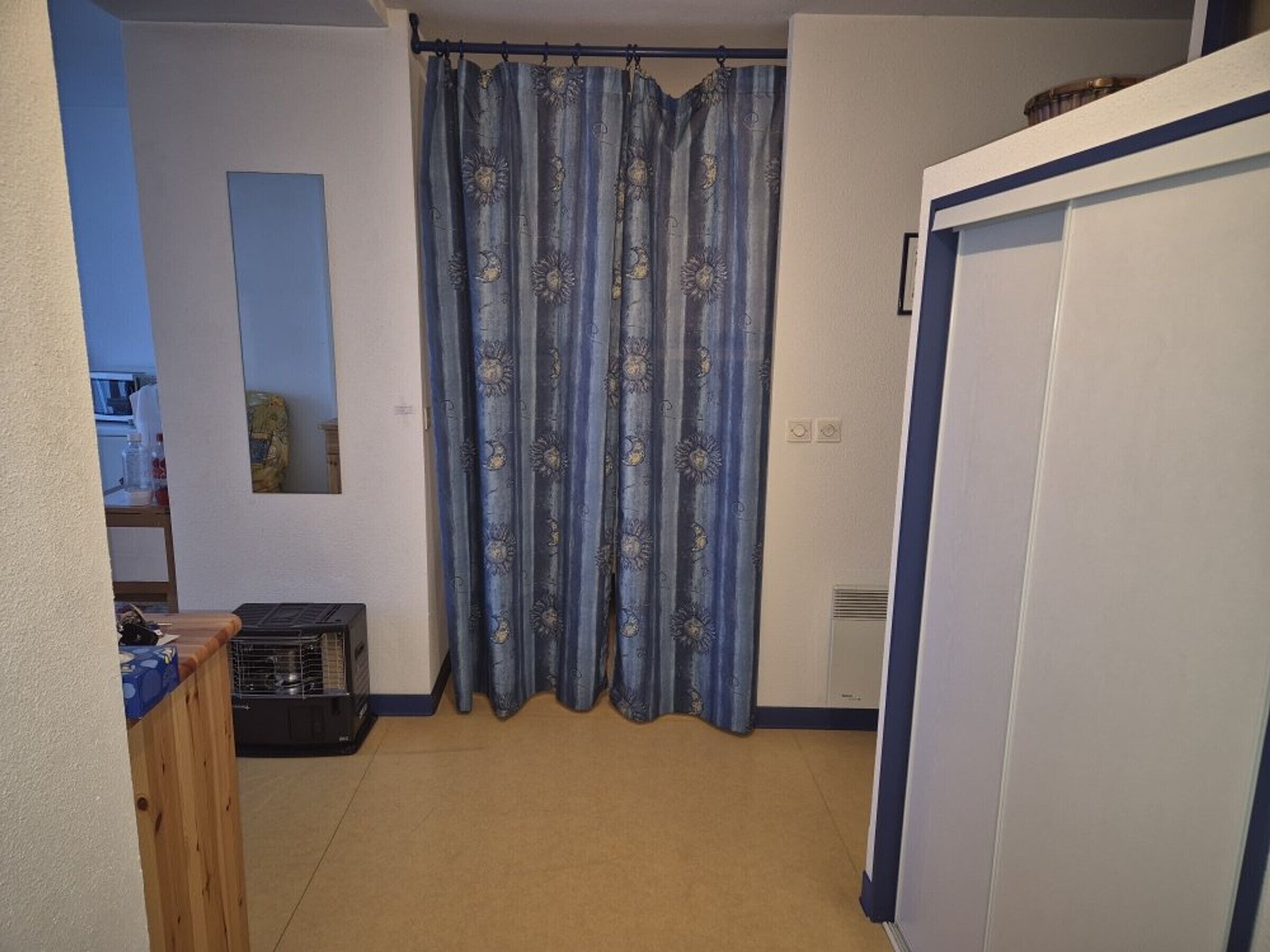 Ein kleiner, schmaler Raum mit Vorhang, Heizkörper und Schrank.
