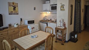 A compact kitchen with a microwave, refrigerator, and sink. There's a dining table with chairs and a small cabinet. - Charming T2bis 4-6 people, near center, Cauterets (Cauterets)
