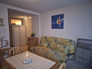 A dining area with a table, chairs, a sofa, and a painting of sailboats on the wall. - Charming T2bis 4-6 people, near center, Cauterets (Cauterets)