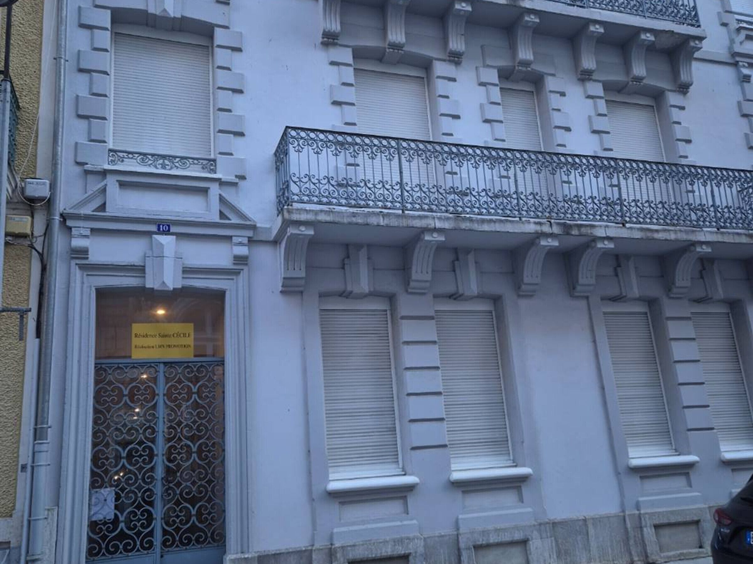 A building with a white facade, ornate iron balcony railings, and a sign indicating a residence.