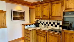 Een keuken met houten kastjes, een betegelde spatwand en een inbouwoven.